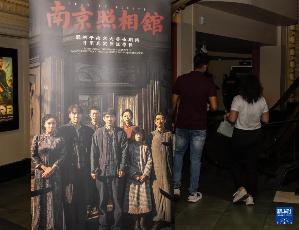 8月15日，在美國(guó)紐約市一家電影院，觀眾經(jīng)過(guò)電影《南京照相館》的海報(bào)。新華社發(fā)（周煥新攝）