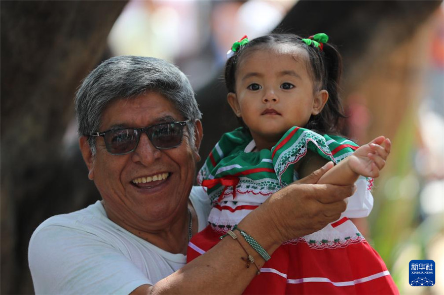 9月16日，在墨西哥瓦哈卡州的瓦哈卡市中心，一名小女孩身著國(guó)旗顏色的傳統(tǒng)民族服裝，在家人帶領(lǐng)下參加獨(dú)立日慶?；顒?dòng)。新華社記者 李夢(mèng)馨 攝