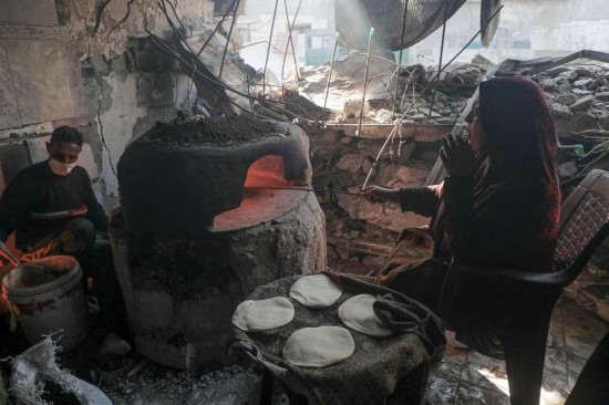 12月15日，在加沙地帶中部城市代爾拜拉赫，巴勒斯坦人在被毀壞的房屋中烤制大餅。新華社發(fā)（里澤克·阿卜杜勒賈瓦德攝）