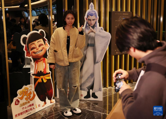 3月14日，在日本東京，一名觀眾在《哪吒之魔童鬧?！啡毡臼子呈胶笈c電影宣傳板合影。新華社記者 賈浩成 攝