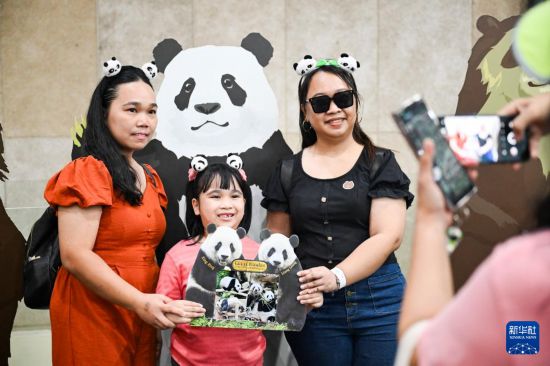 5月17日，在馬來西亞吉隆坡的國家動物園，人們在大熊貓館內(nèi)舉著大熊貓“興興”和“靚靚”的牌子合影。新華社記者 程一恒 攝