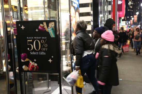 2024年11月29日，在美國紐約曼哈頓島的一家商場外，人們經(jīng)過“黑色星期五”促銷廣告牌。新華社記者劉亞南攝
