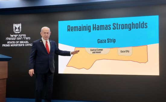 　　8月10日，以色列總理內(nèi)塔尼亞胡在耶路撒冷舉行的記者會上用手指向屏幕中的加沙地帶地圖（手機照片）。新華社記者馮國芮攝