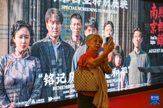 　8月24日，在馬來(lái)西亞吉隆坡，一名觀眾觀影后同《南京照相館》海報(bào)合影留念。新華社記者 程一恒 攝