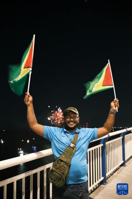 　　10月5日，在圭亞那首都喬治敦，一名男子揮舞圭亞那國旗在巴拉特·賈格迪奧-德梅拉拉河大橋上與身后的煙花合影。新華社記者 許詠政 攝